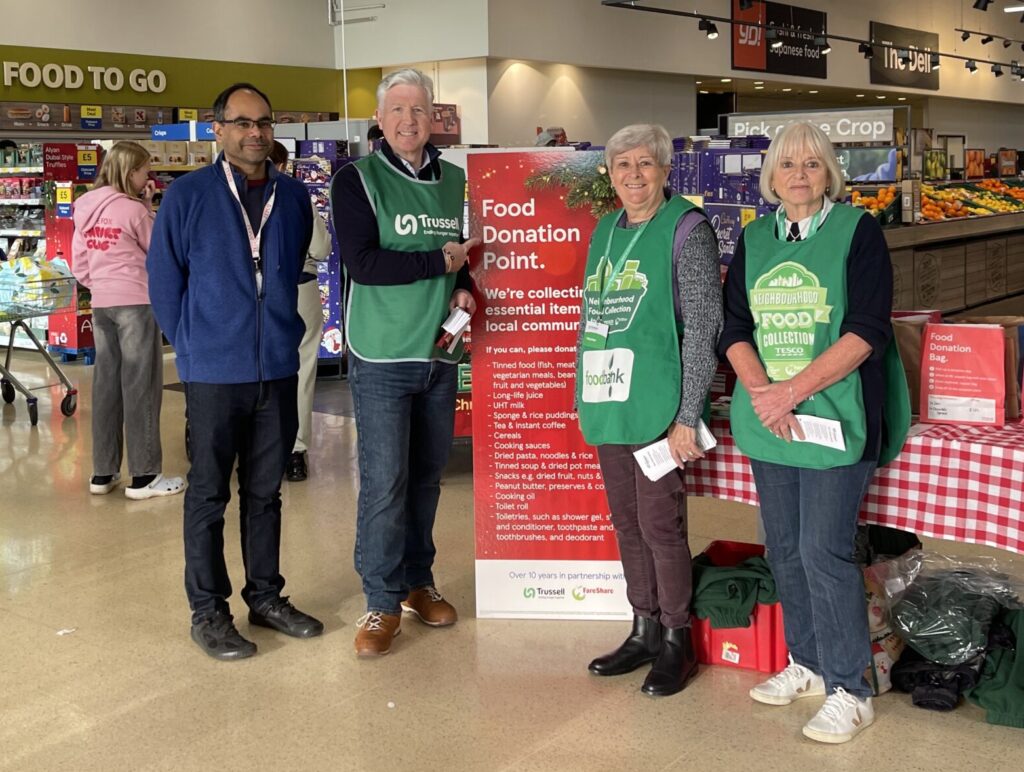 Volunteers from Slough Foodbank stand by a Food Donation Point poster at Tesco