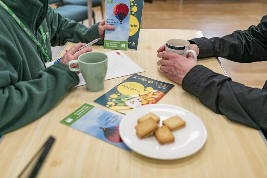 Two people sitting across a table on which are some leaflets and biscuits