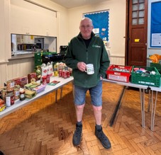Male volunteer stands in front of tables loaded with food items